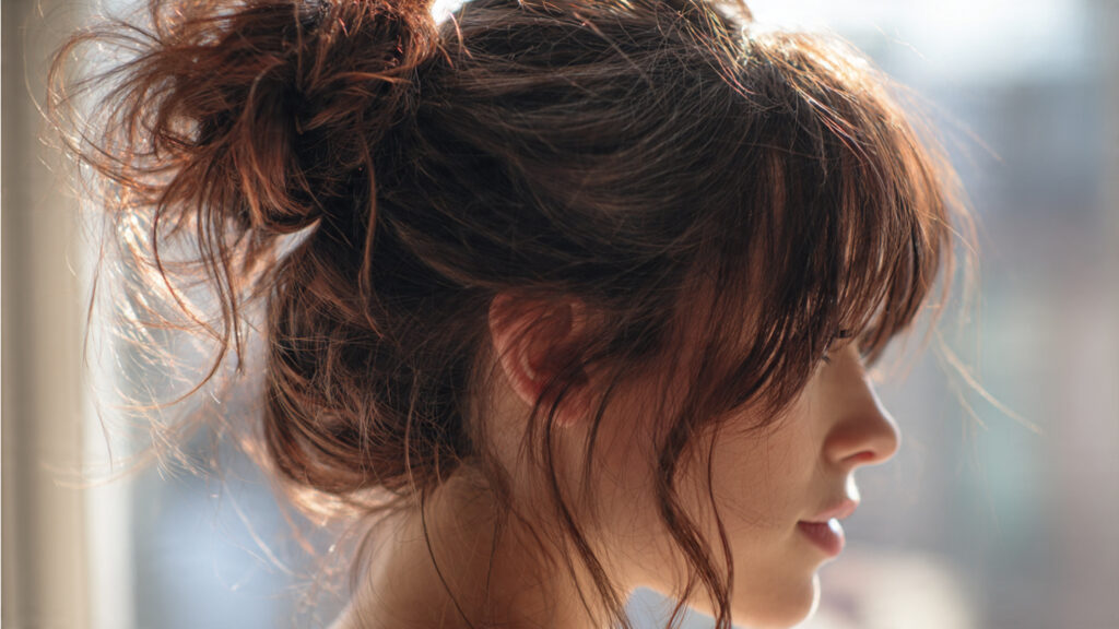 Messy bun hairstyle with wispy bangs.